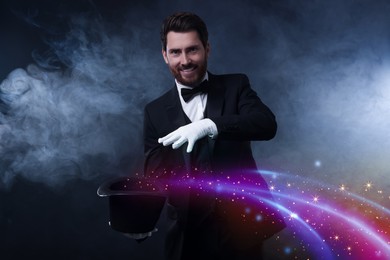 Smiling magician showing trick with top hat on dark background