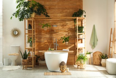 Photo of Stylish bathroom interior with white tub and green houseplants near wooden wall. Idea for design
