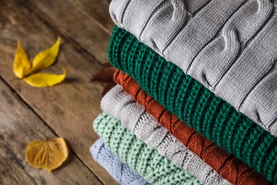 Photo of Stack of warm knitted clothes and autumn leaves on wooden background, above view