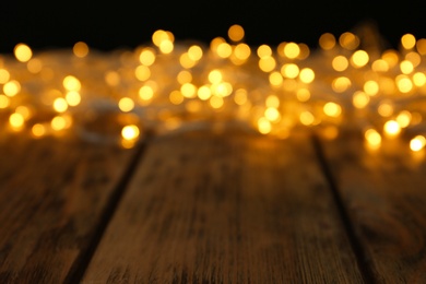 Blurred view of glowing Christmas lights on wooden table