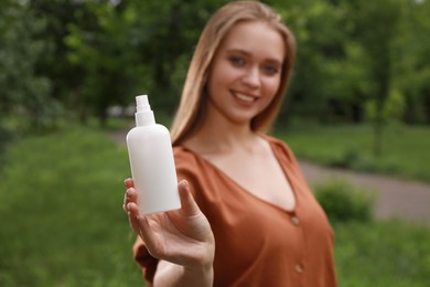 Photo of Woman with insect repellent spray in park, focus on bottle. Tick bites prevention