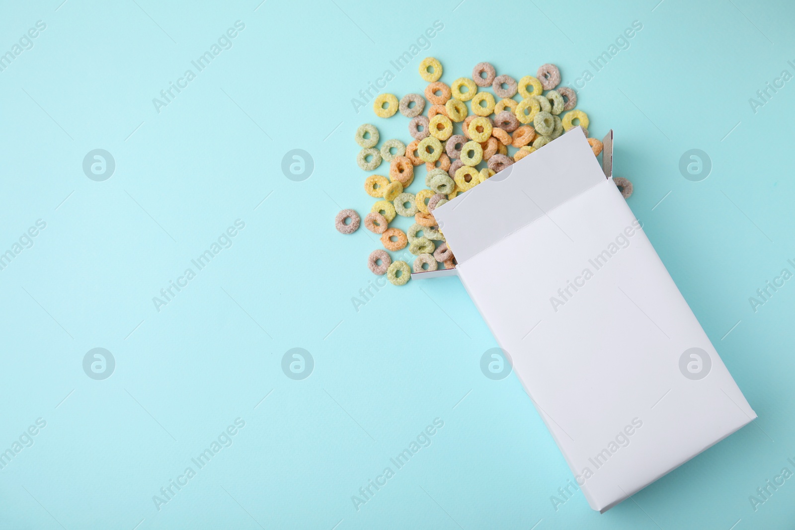 Photo of Paper box with tasty cereal rings on light blue background, flat lay. Space for text