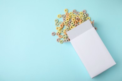 Photo of Paper box with tasty cereal rings on light blue background, flat lay. Space for text