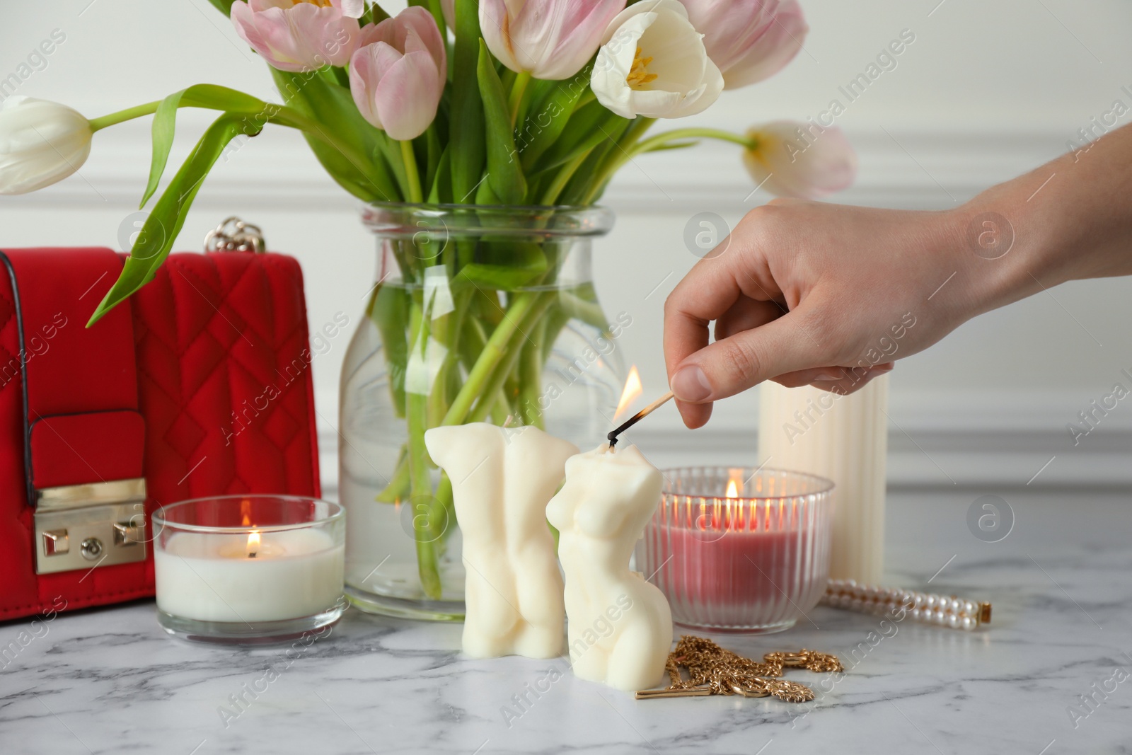 Photo of Woman lighting female body shaped candle on white marble table, closeup. Stylish decor