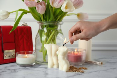 Photo of Woman lighting female body shaped candle on white marble table, closeup. Stylish decor