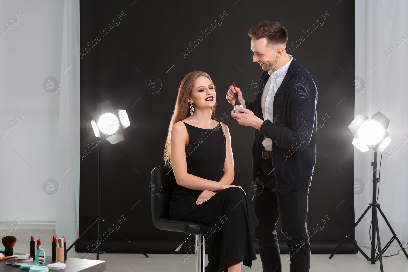 Photo of Professional makeup artist working with beautiful young woman in photo studio