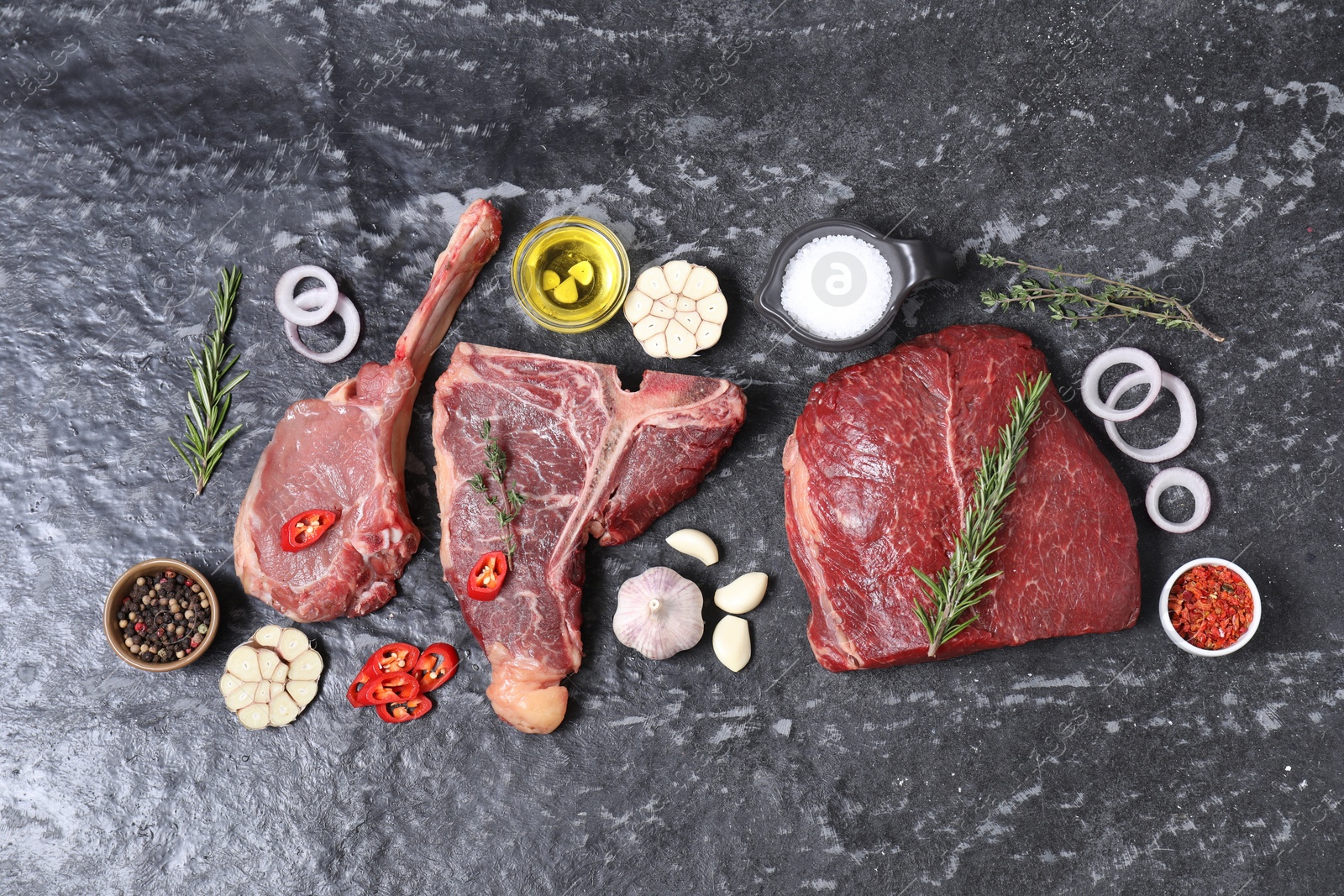 Photo of Fresh raw beef cuts and different spices on grey textured table, flat lay