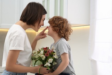 Photo of Happy woman with her cute son and bouquet of beautiful flowers in kitchen, space for text. Mother's day celebration