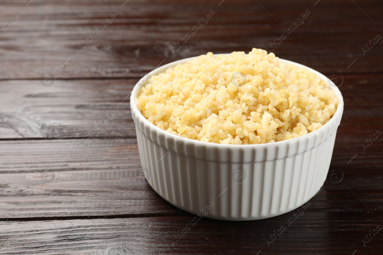 Photo of Delicious bulgur in bowl on wooden table, closeup. Space for text