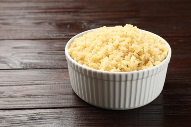 Photo of Delicious bulgur in bowl on wooden table, closeup. Space for text