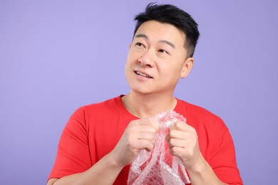 Asian man with bubble wrap on purple background