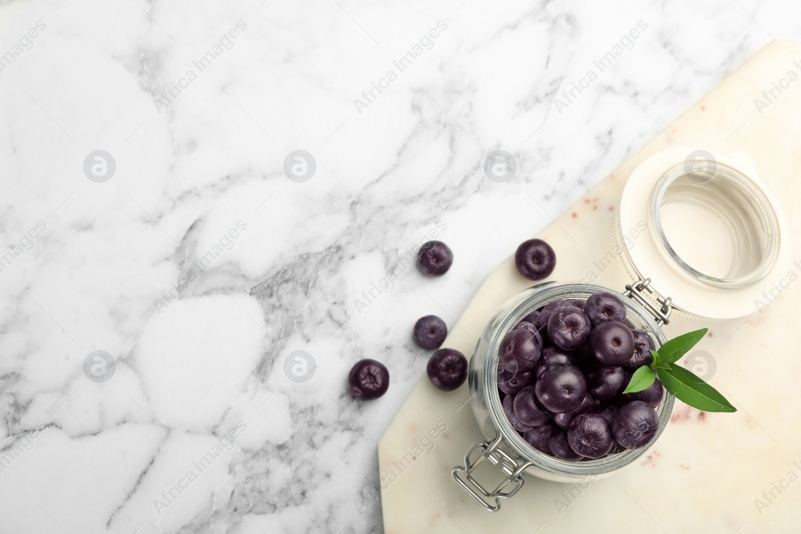 Photo of Jar of fresh acai berries with board on marble table, flat lay. Space for text