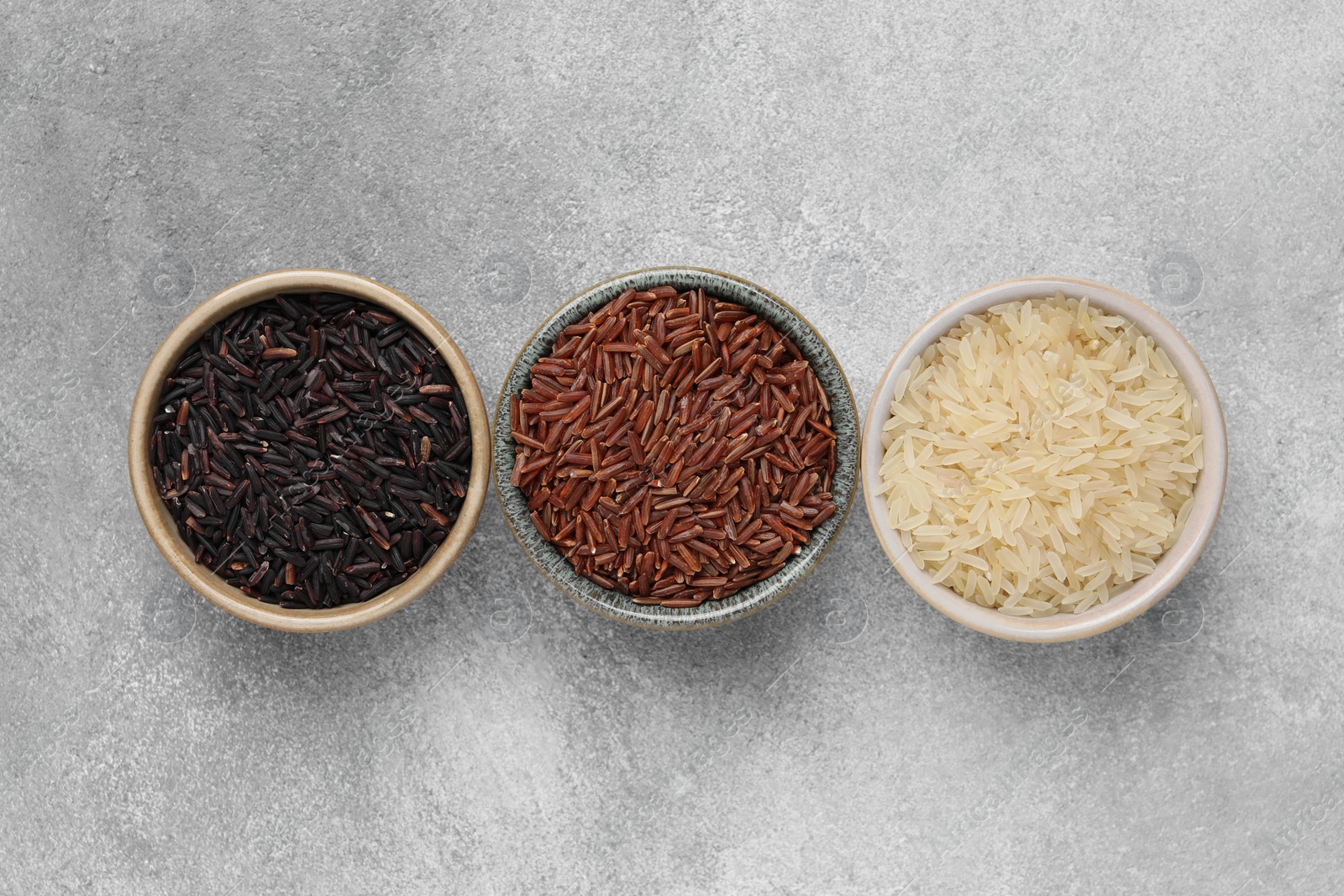 Photo of Bowls with different sorts of rice on grey table, flat lay