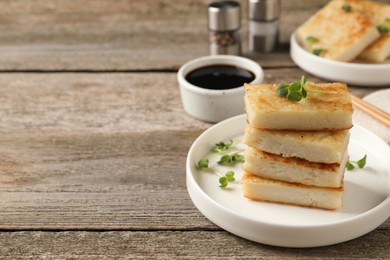 Photo of Delicious turnip cake with microgreens served on wooden table. Space for text
