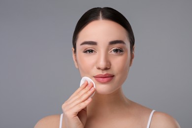 Photo of Beautiful woman removing makeup with cotton pad on gray background