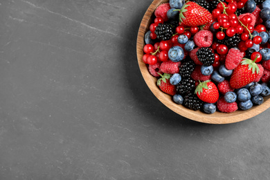 Mix of different fresh berries in bowl on grey table, top view. Space for text