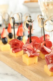 Tasty canapes with cheese and ham on white marble table, closeup