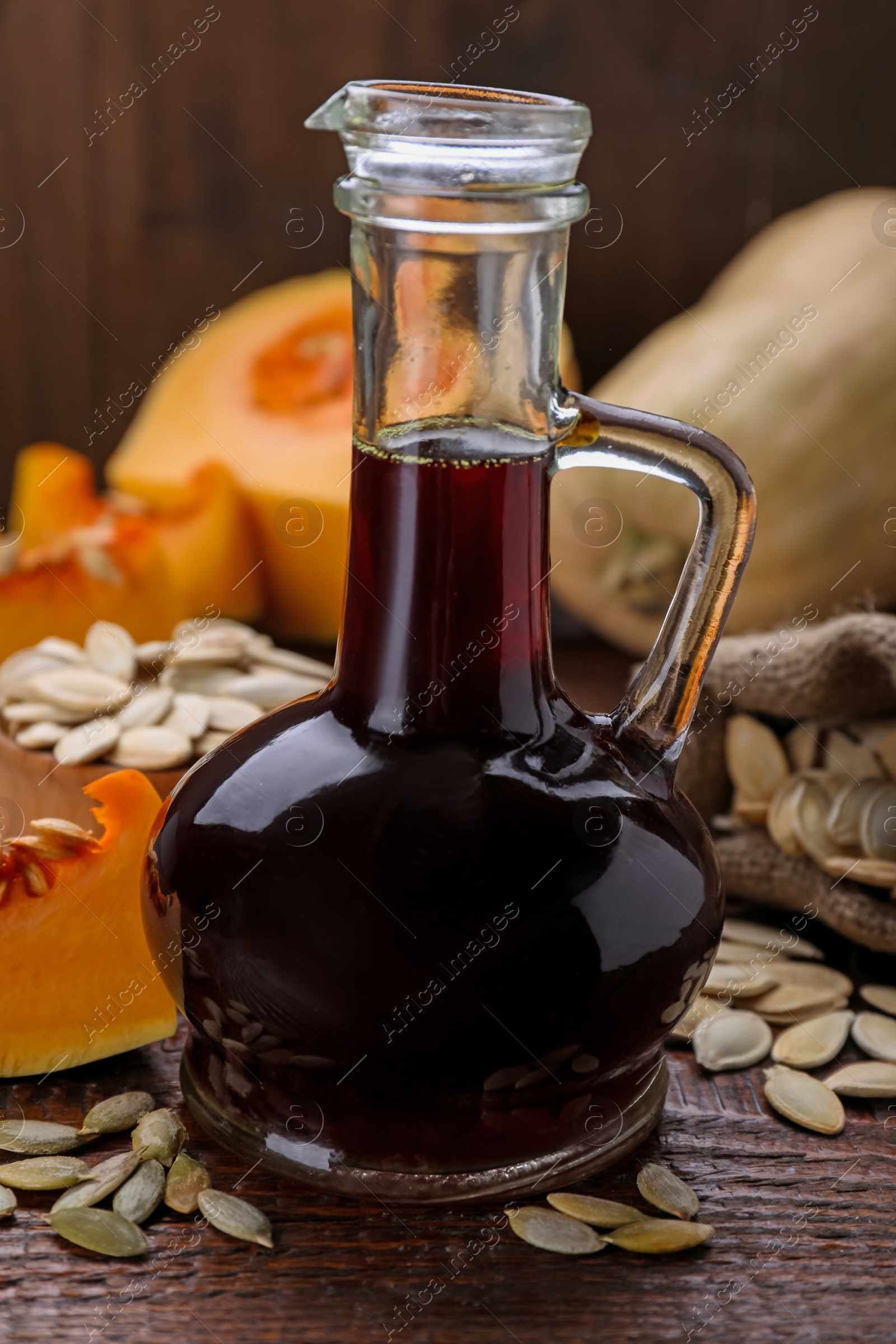 Photo of Fresh pumpkin seed oil in glass jug on wooden table