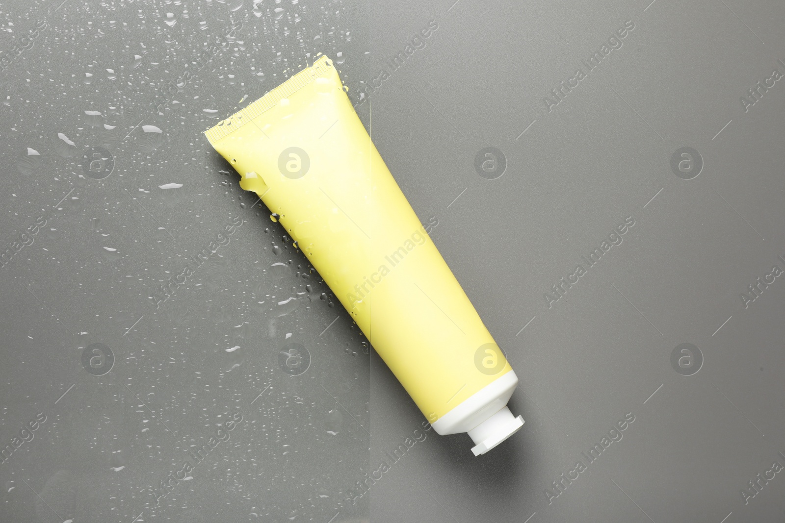 Photo of Tube with moisturizing cream on wet grey surface, top view