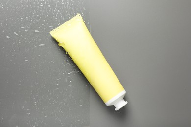 Tube with moisturizing cream on wet grey surface, top view