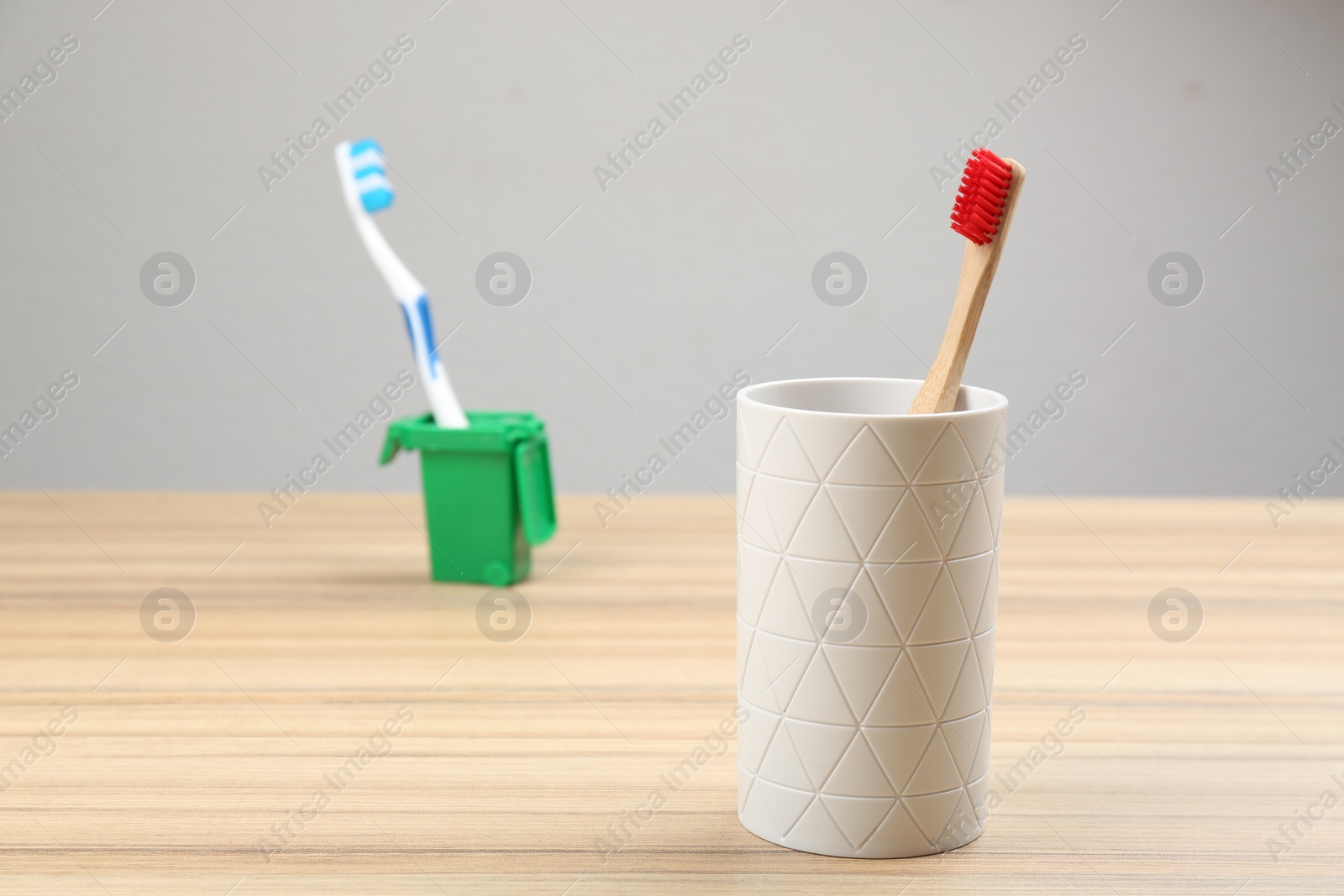 Photo of Natural bamboo toothbrush and plastic one in toy trash can on wooden table