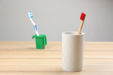 Natural bamboo toothbrush and plastic one in toy trash can on wooden table