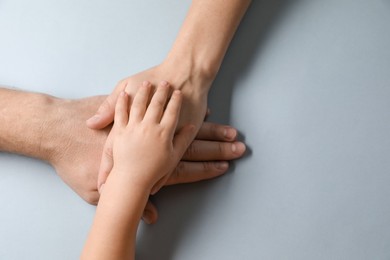 Photo of Parents and child holding hands together on gray background, top view. Space for text