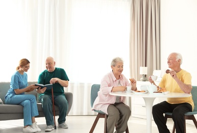 Photo of Nurse assisting elderly man while senior couple having breakfast at retirement home