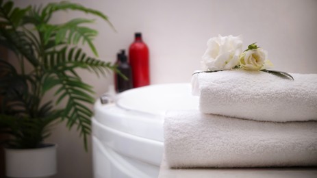 Stacked bath towels and beautiful flowers on table in bathroom, space for text