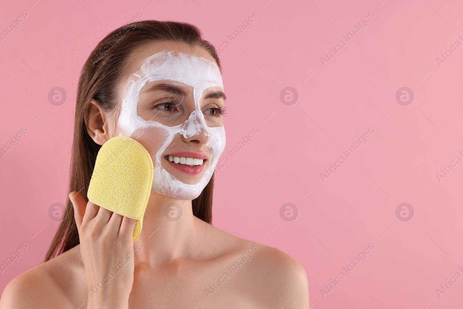 Photo of Happy young woman washing off face mask with sponge on pink background. Space for text