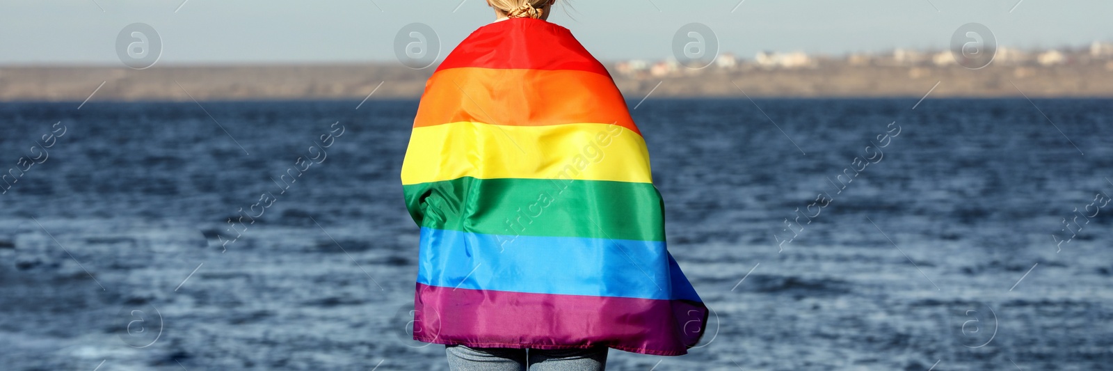 Image of Woman wrapped in bright LGBT flag near river, back view. Banner design