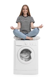 Beautiful young woman meditating on washing machine with laundry against white background