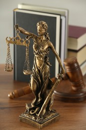 Photo of Figure of Lady Justice, gavel and books on wooden table indoors. Symbol of fair treatment under law