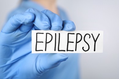 Photo of Doctor holding card with word Epilepsy on light grey background, closeup