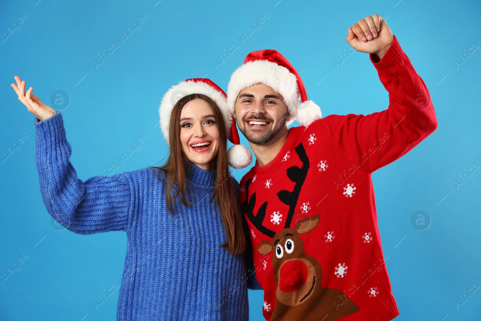 Photo of Couple wearing Christmas sweaters and Santa hats on blue background