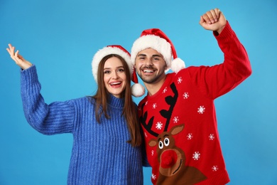 Couple wearing Christmas sweaters and Santa hats on blue background
