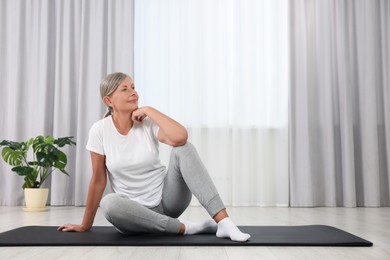 Photo of Happy senior woman sitting on mat at home, space for text. Yoga practice
