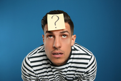 Emotional man with question mark sticker on forehead against blue background