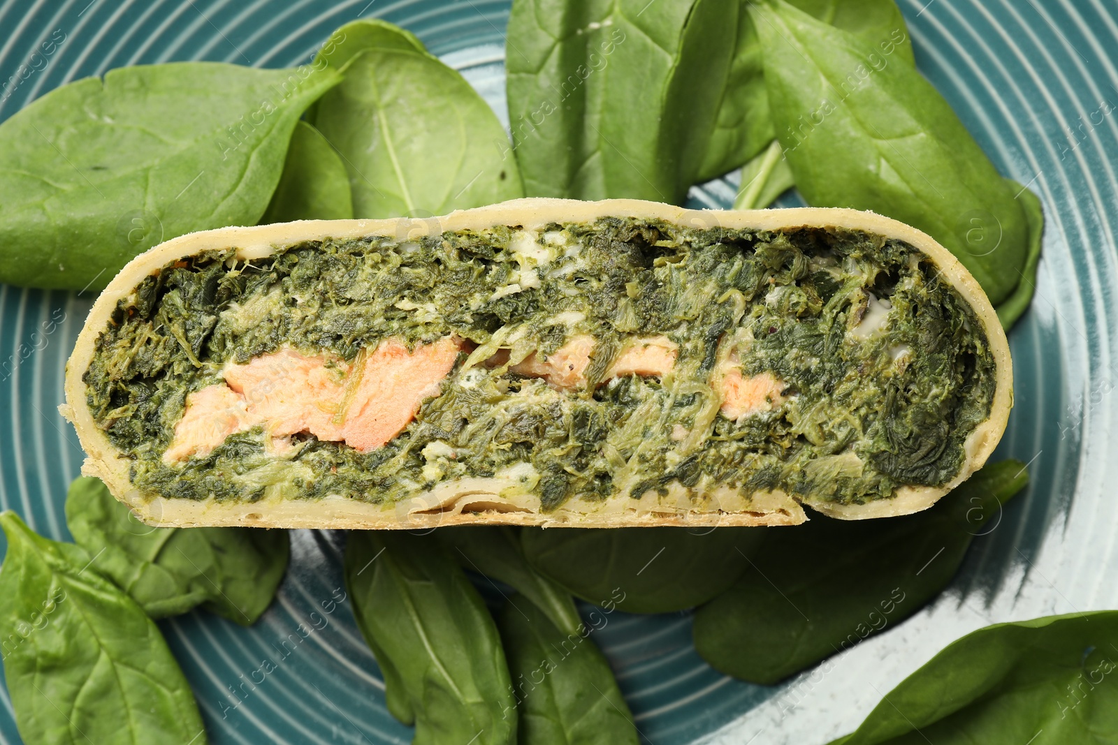 Photo of Piece of delicious strudel with salmon and spinach on plate, top view