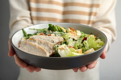 Photo of Woman with bowl of delicious fresh Caesar salad on white background, closeup