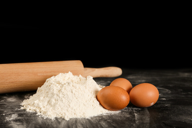 Photo of Raw eggs, flour and rolling pin on black background. Baking pie