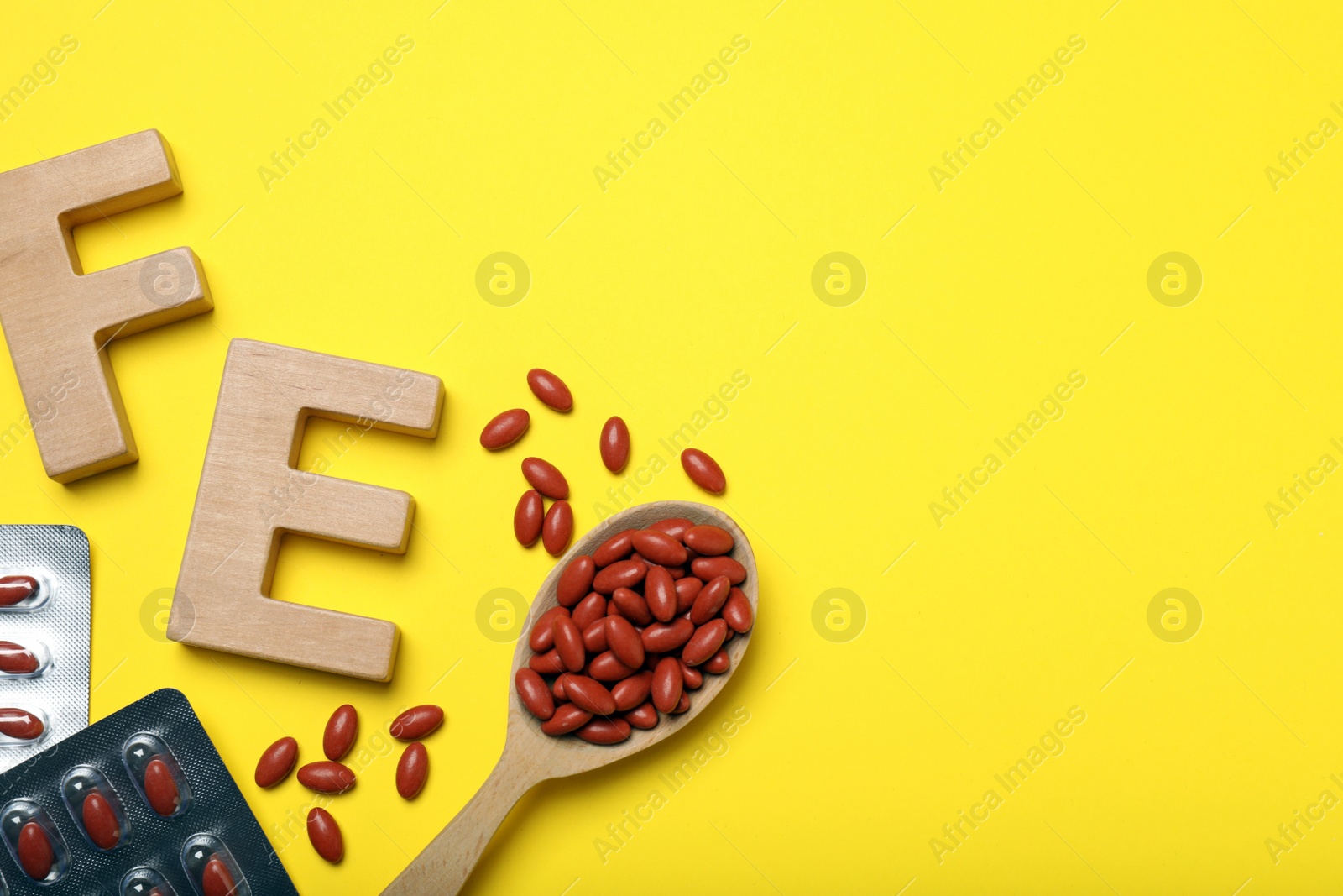 Photo of Wooden letters FE and pills on yellow background, flat lay with space for text. Anemia treatment