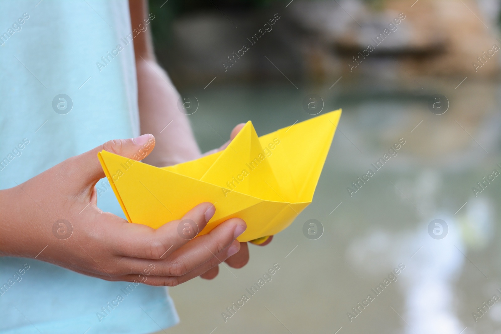 Photo of Little girl holding yellow paper boat outdoors, closeup