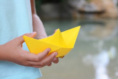 Little girl holding yellow paper boat outdoors, closeup