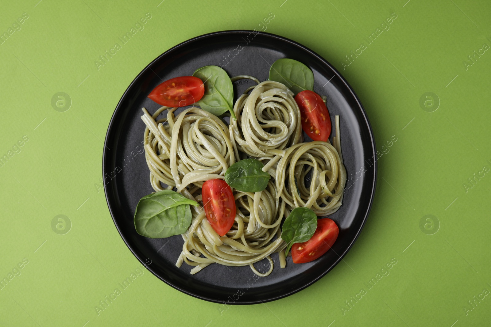 Photo of Tasty pasta with spinach, sauce and tomatoes on green table, top view