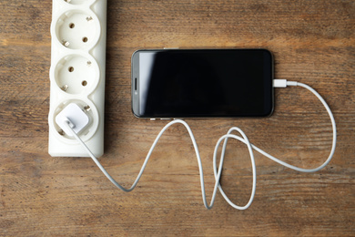 Smartphone charging with cable on wooden table, flat lay