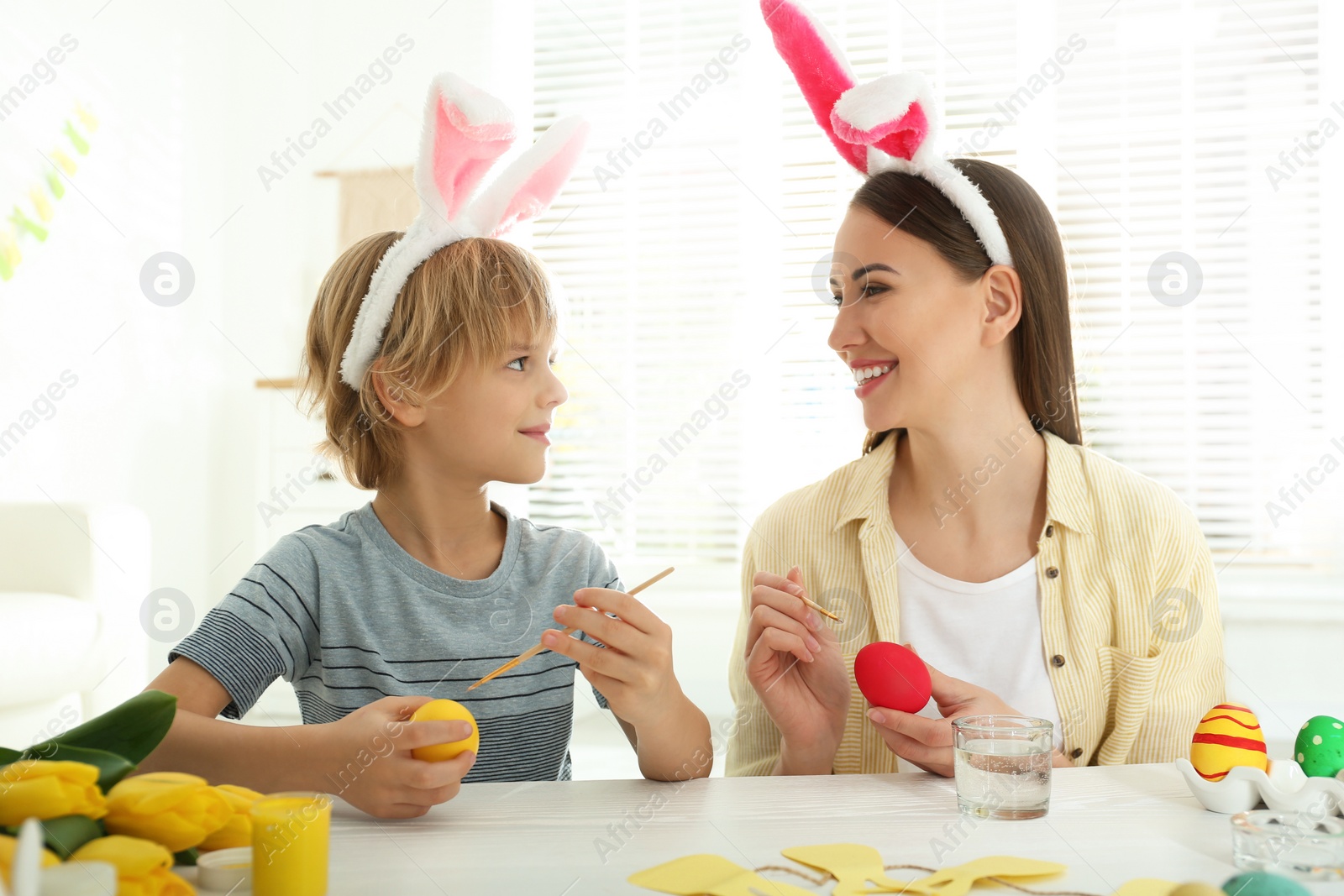 Photo of Happy mother and son with bunny ears headbands painting Easter eggs at home