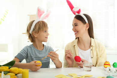 Photo of Happy mother and son with bunny ears headbands painting Easter eggs at home