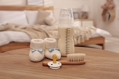 Photo of Baby booties, pacifier, feeding bottle and brush on wooden table in bedroom. Maternity leave concept