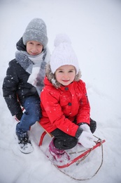 Photo of Cute little children sitting on sleigh in snowy park, above view